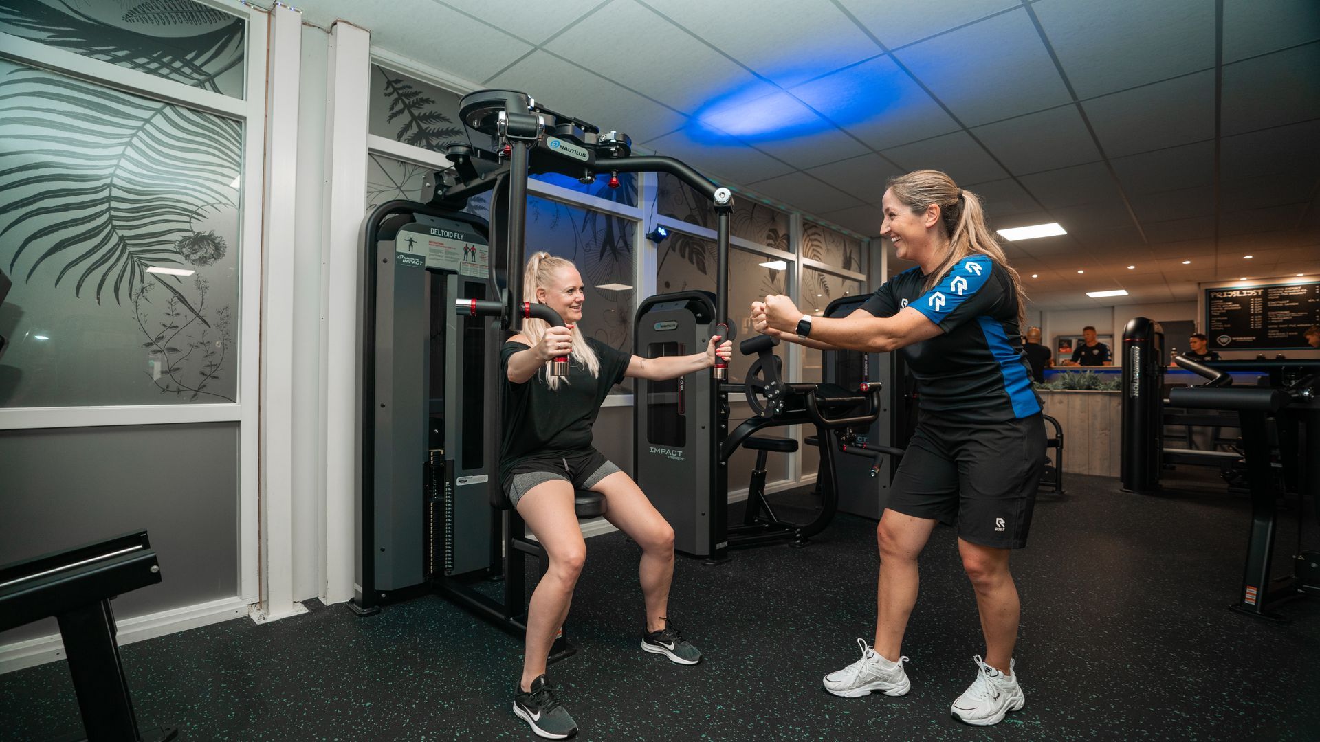 Een vrouw traint samen met een trainer in de sportschool met behulp van een gewichtsmachine.