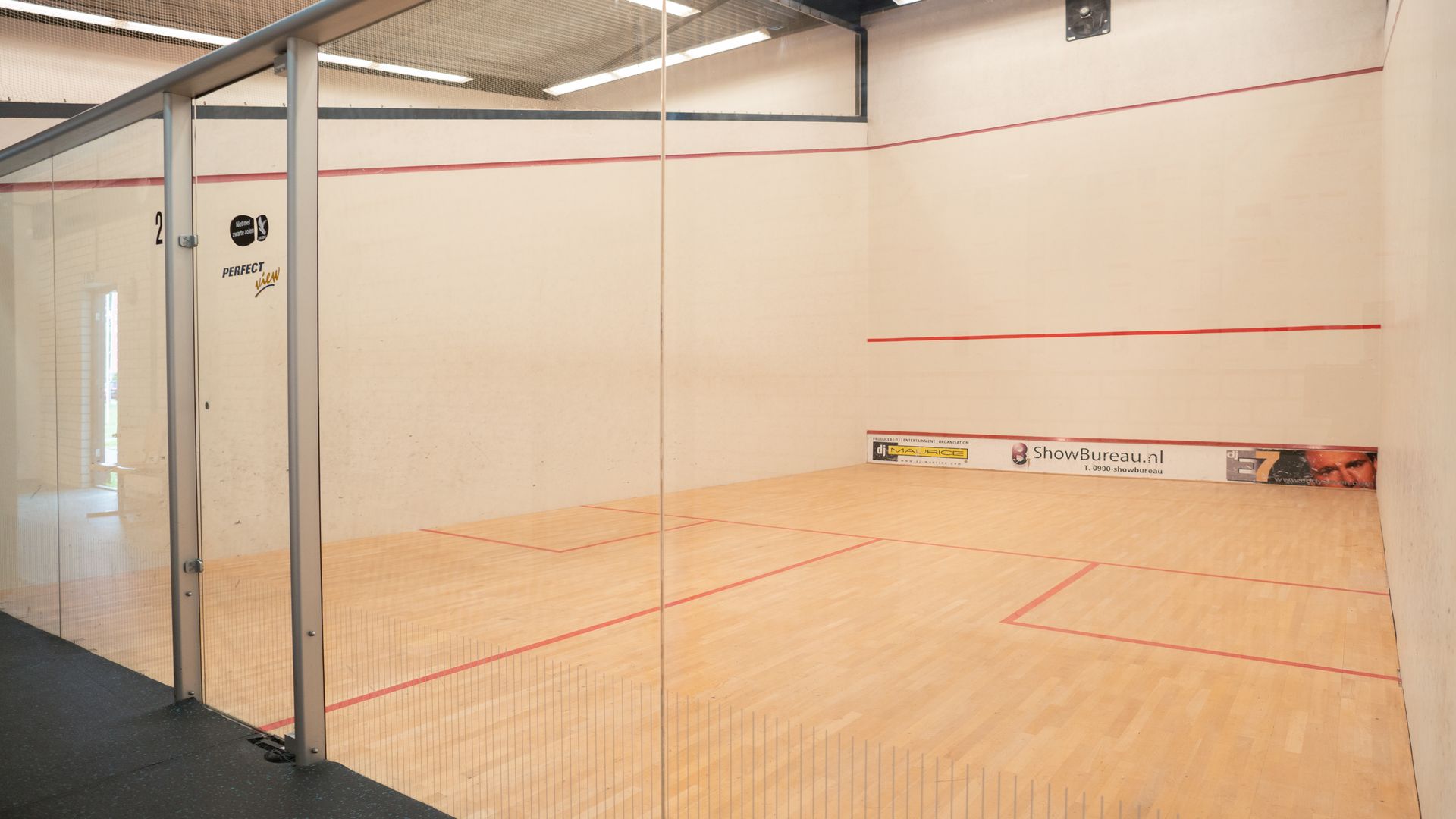 Lege squashbaan met glazen wand, rode lijnen op de vloer en de muren.