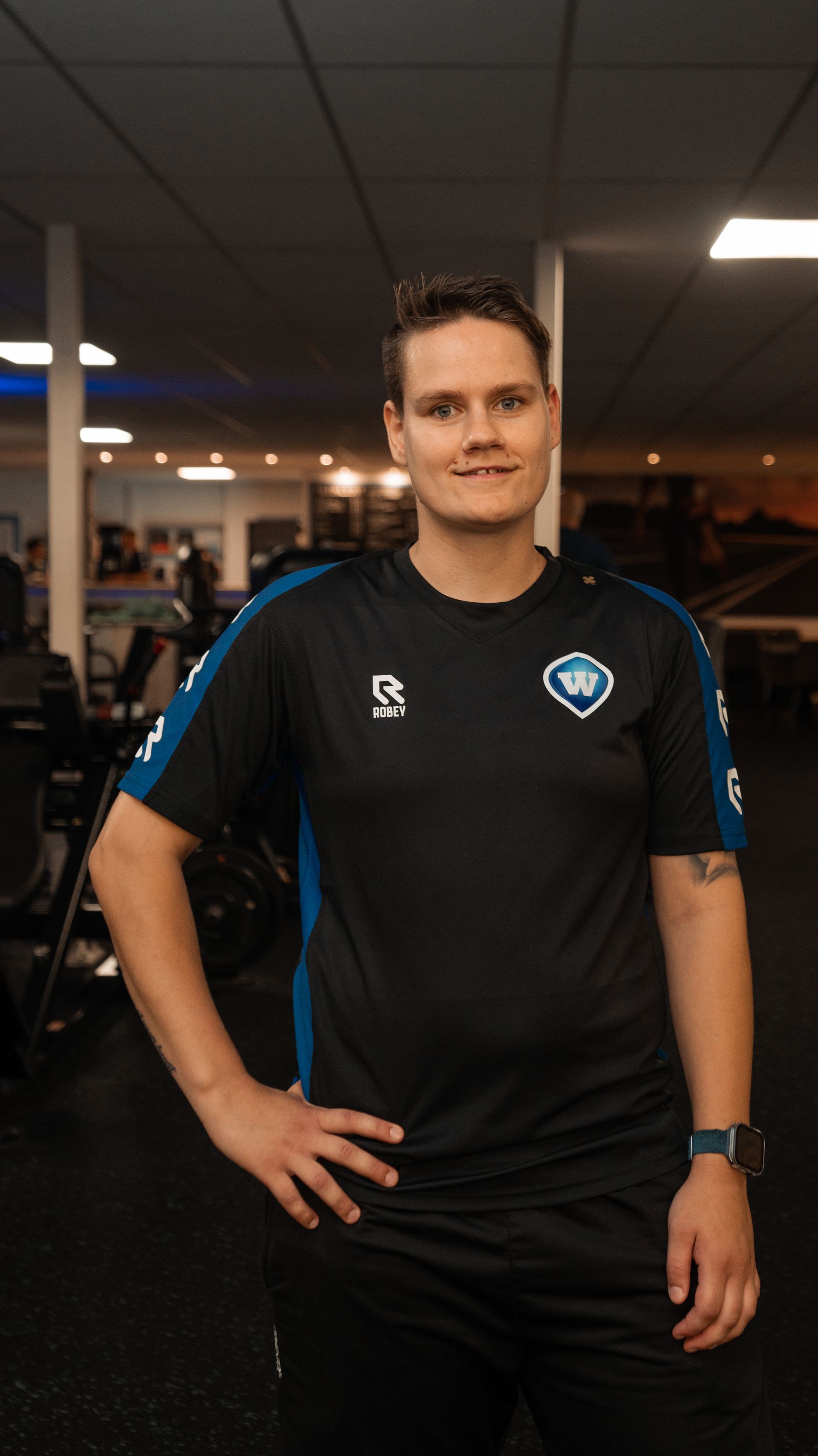 Man in een sporttenue in een sportschool, hand in zijn zij, lachend.