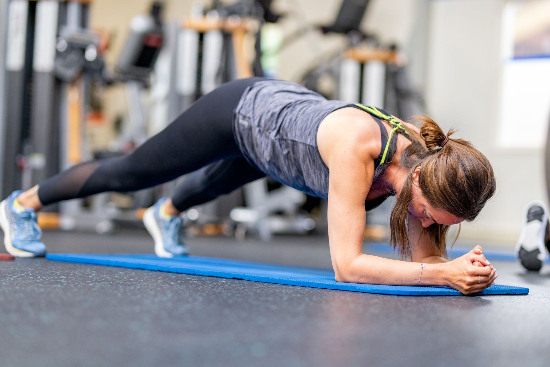 Vrouw in sportkleding doet een plank op een blauwe mat in een sportschool.