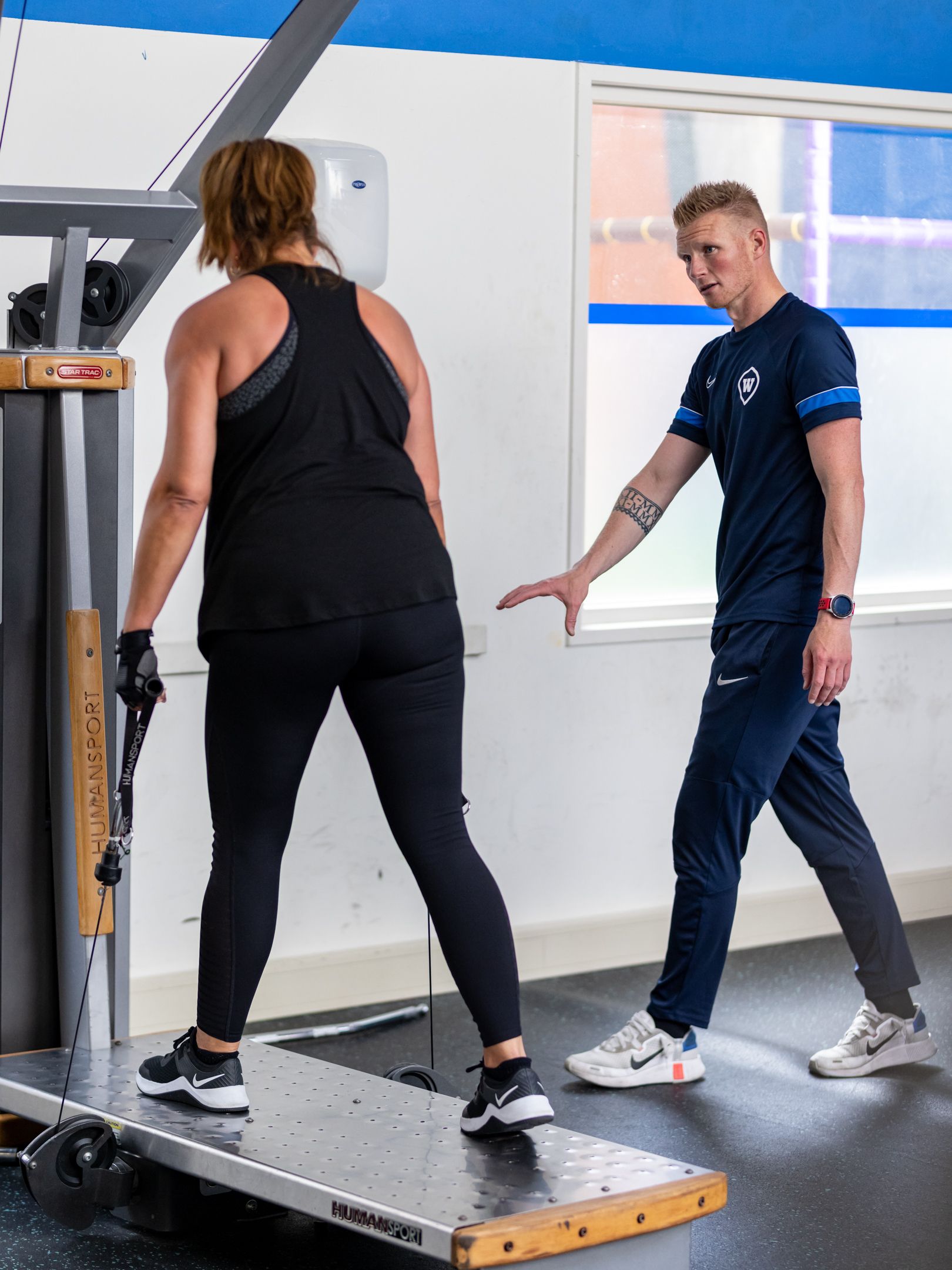 Vrouw gebruikt een gewichtsapparaat, onder begeleiding van een trainer, in een sportschool.