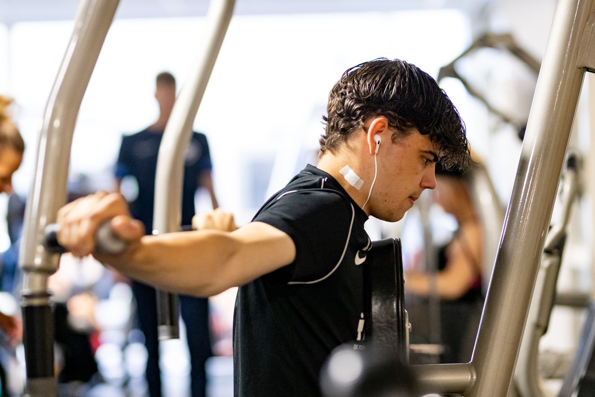 Man gebruikt een borstdrukmachine in de sportschool, draagt ​​oordopjes en een zwart shirt.