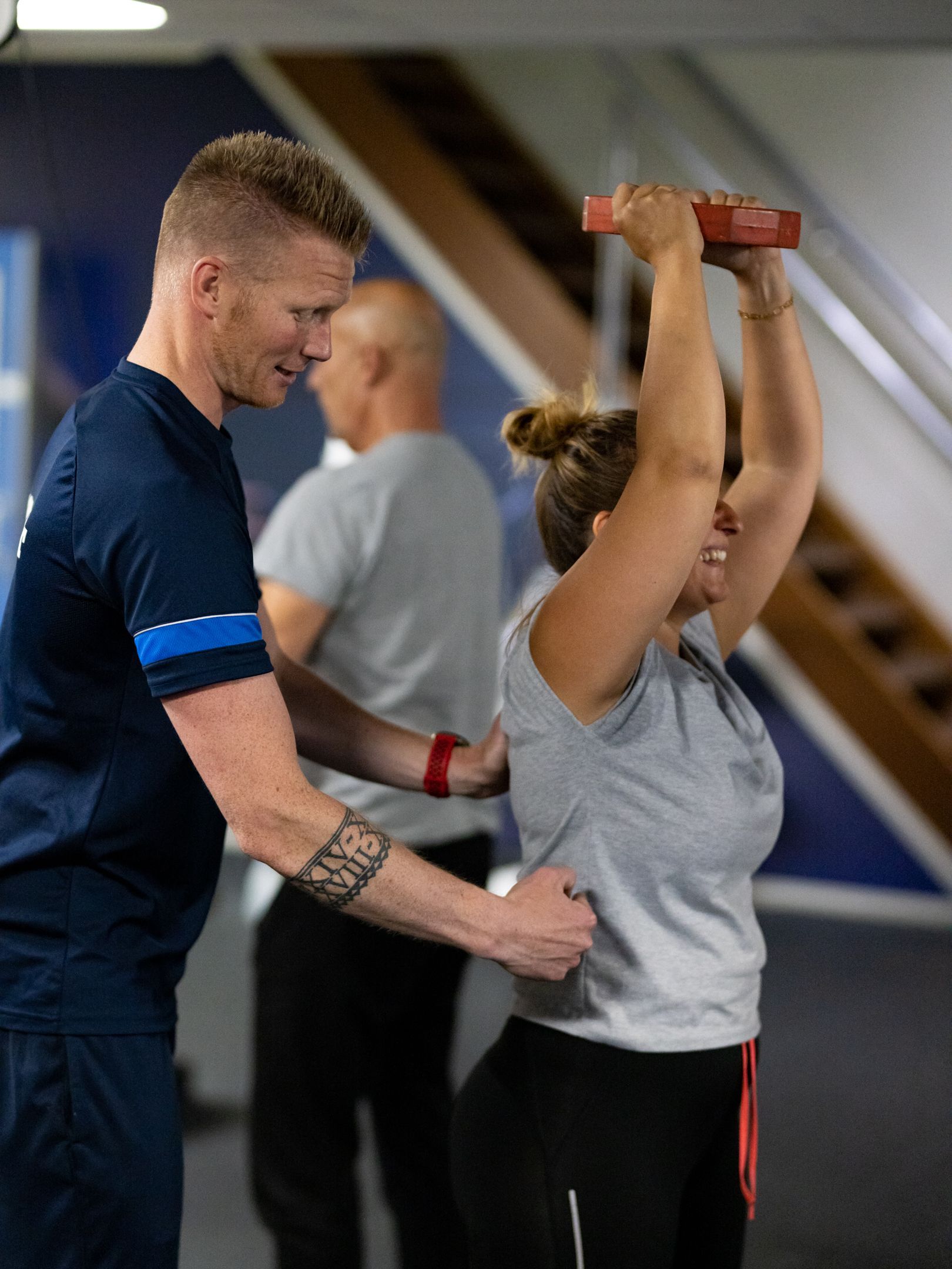 Trainer helpt vrouw bij oefeningen met gewichten boven haar hoofd in de sportschool.