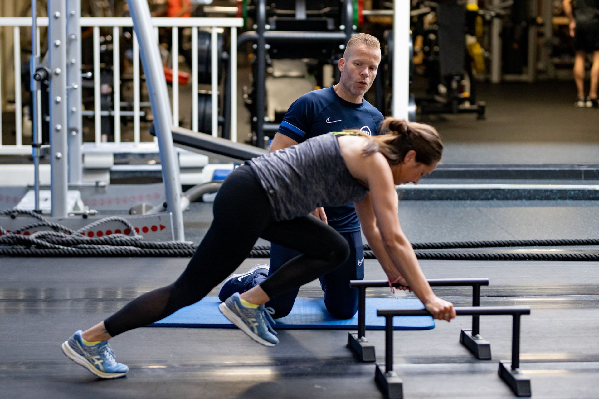 Een vrouw doet samen met een trainer oefeningen in de sportschool. Ze stapt over kleine hindernissen.