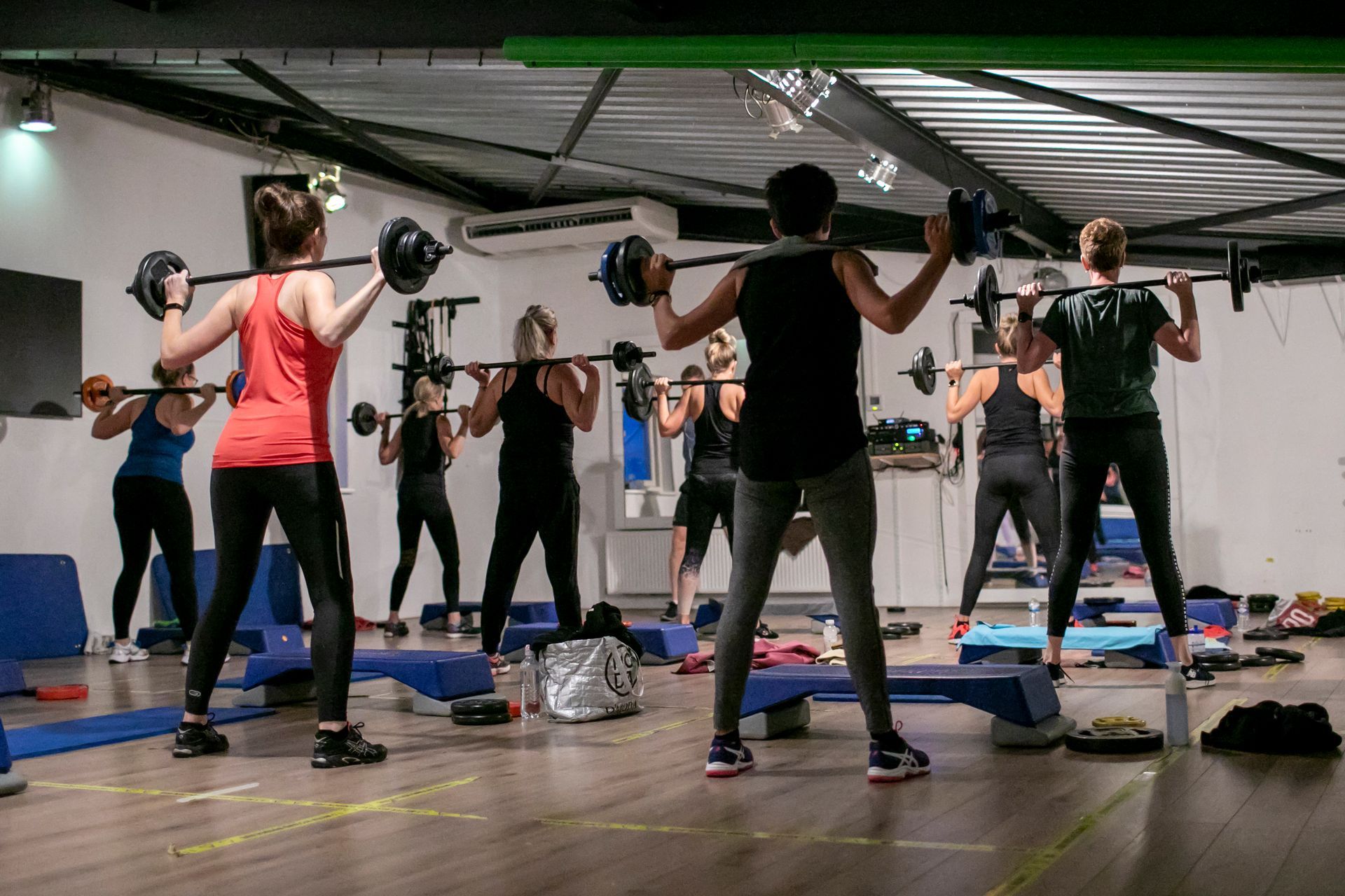 Mensen in een sportschool die gewichten heffen met halters op hun schouders, binnen.