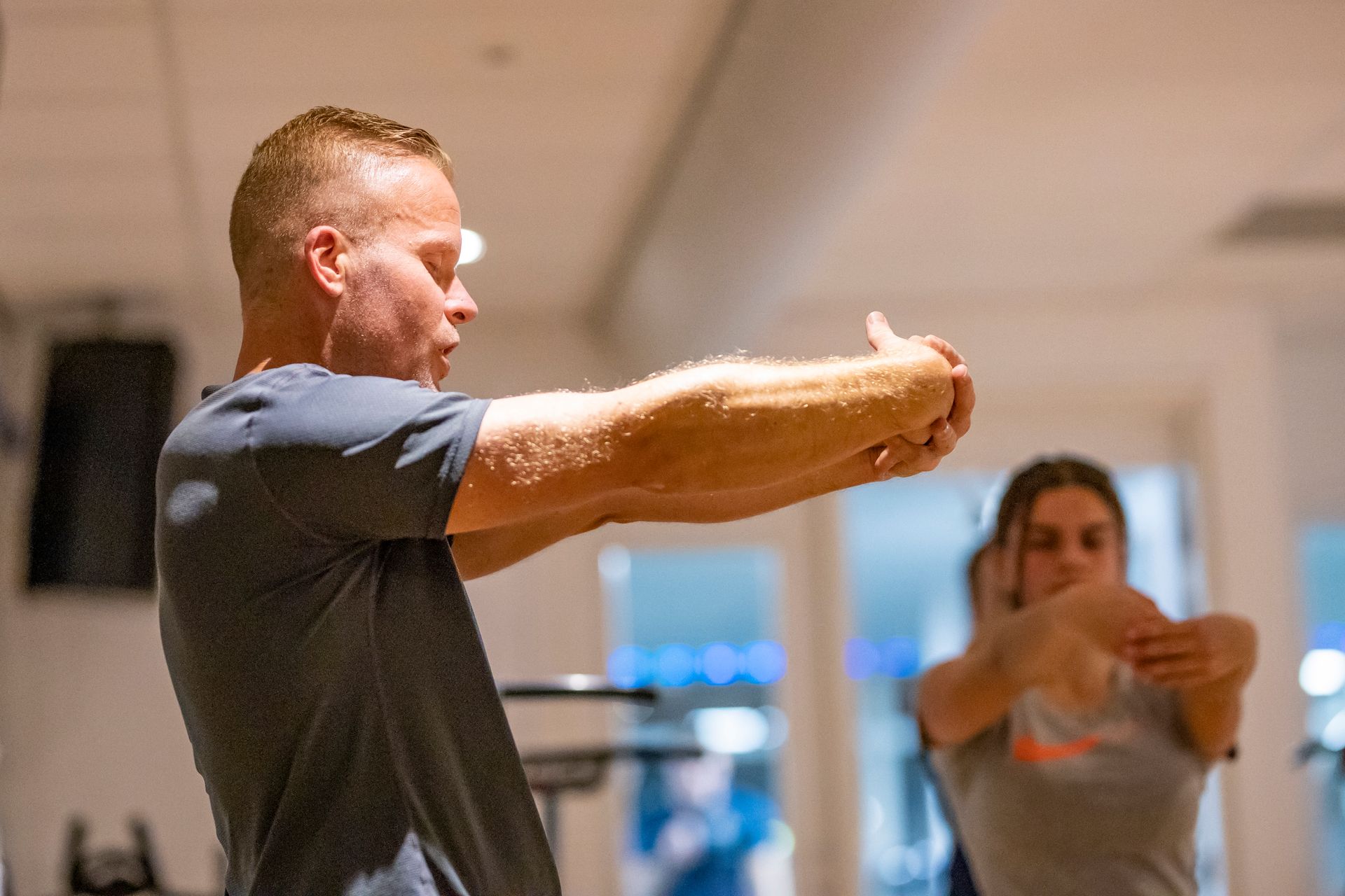 Vrouw doet een core-oefening op een blauwe mat in een sportschool, benen omhoog, handen achter haar hoofd.