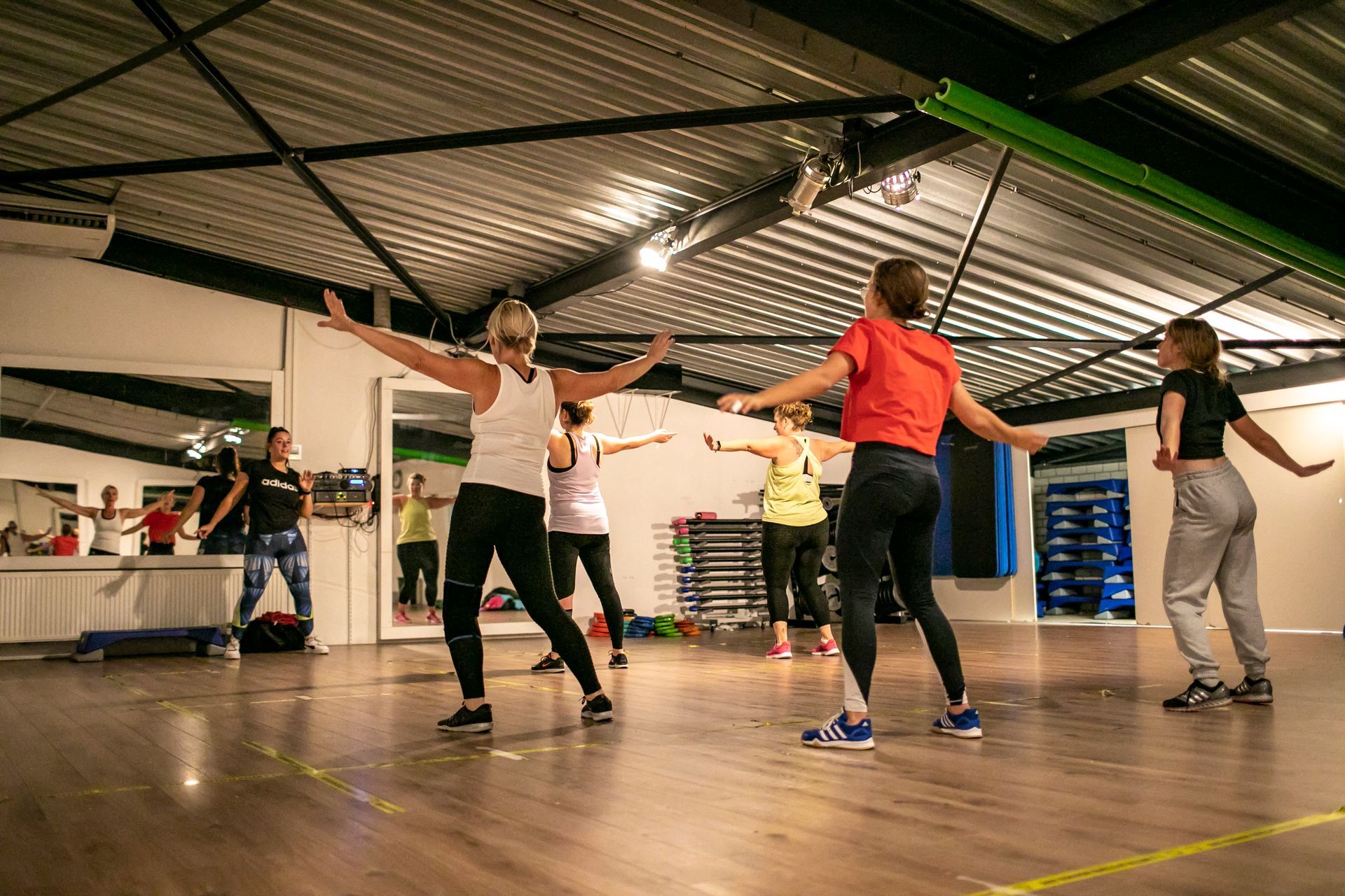 Mensen in een dansles, met uitgestrekte armen, dansen in een studio met een spiegelwand.