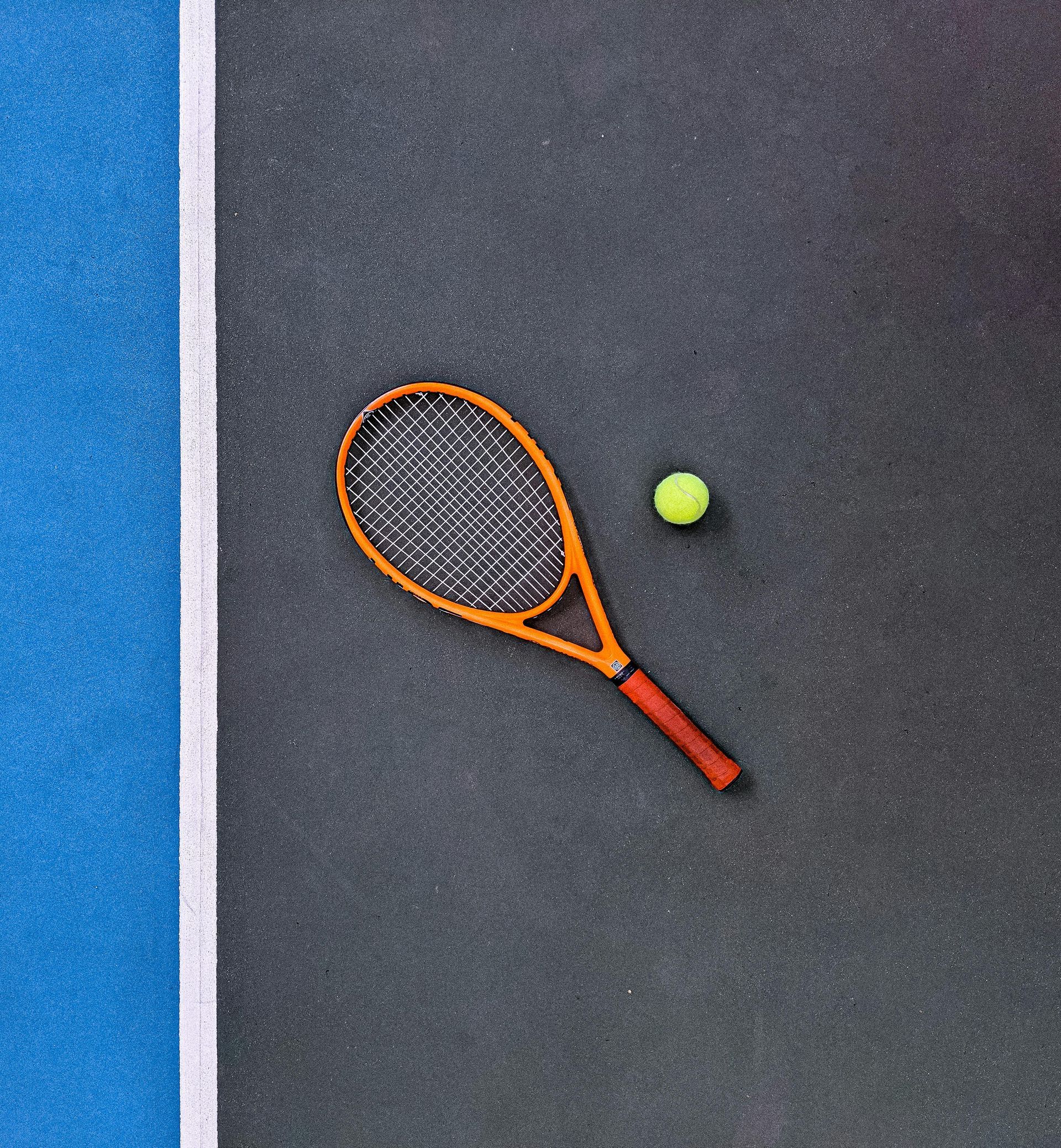Tennisracket en bal op een donkere baan met een blauw-witte lijn.
