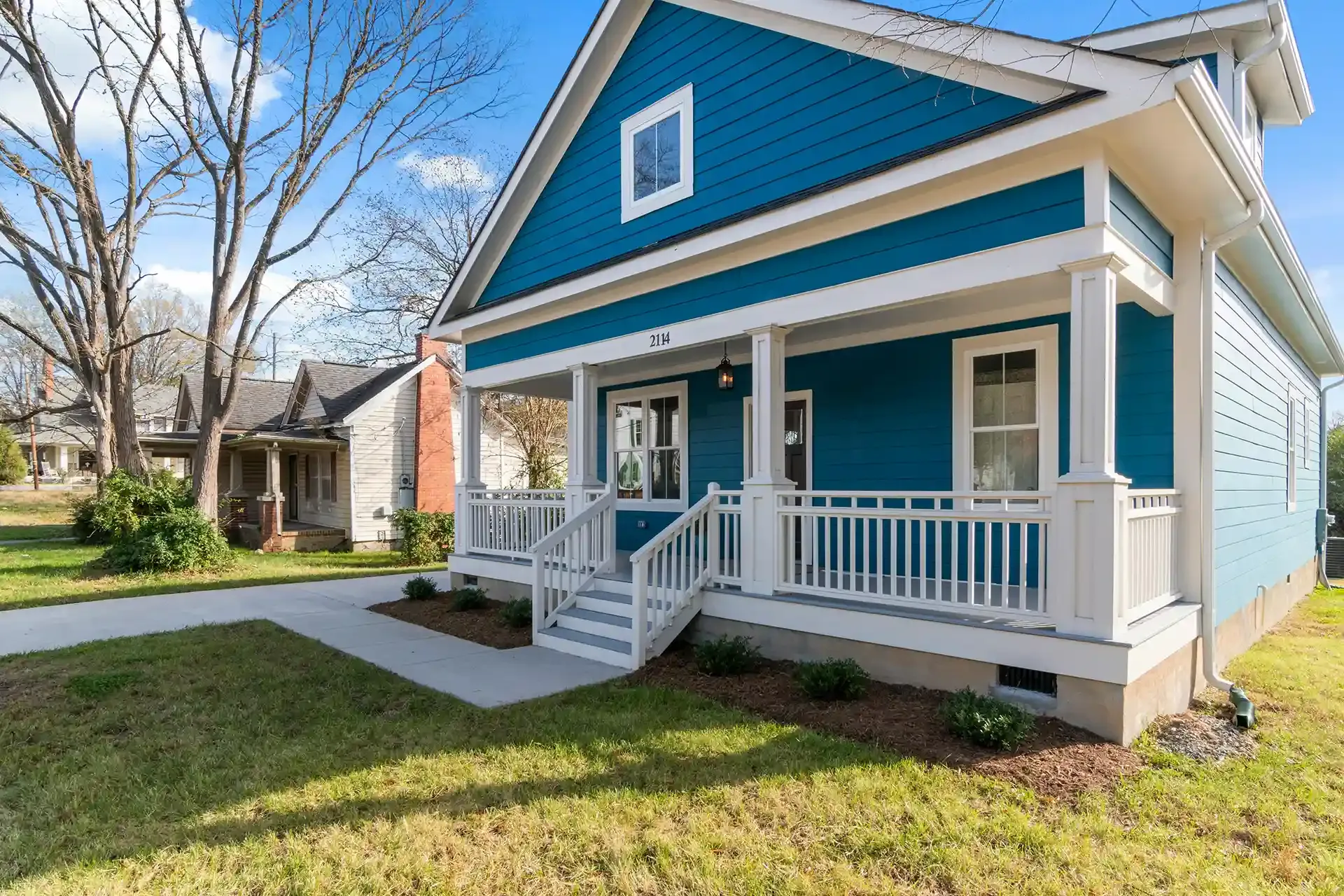 Blue house with white trim and a front porch in a sunny suburban yard
