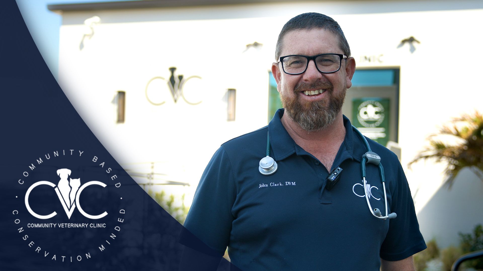 Man with a beard, glasses, and stethoscope smiles outside building with 