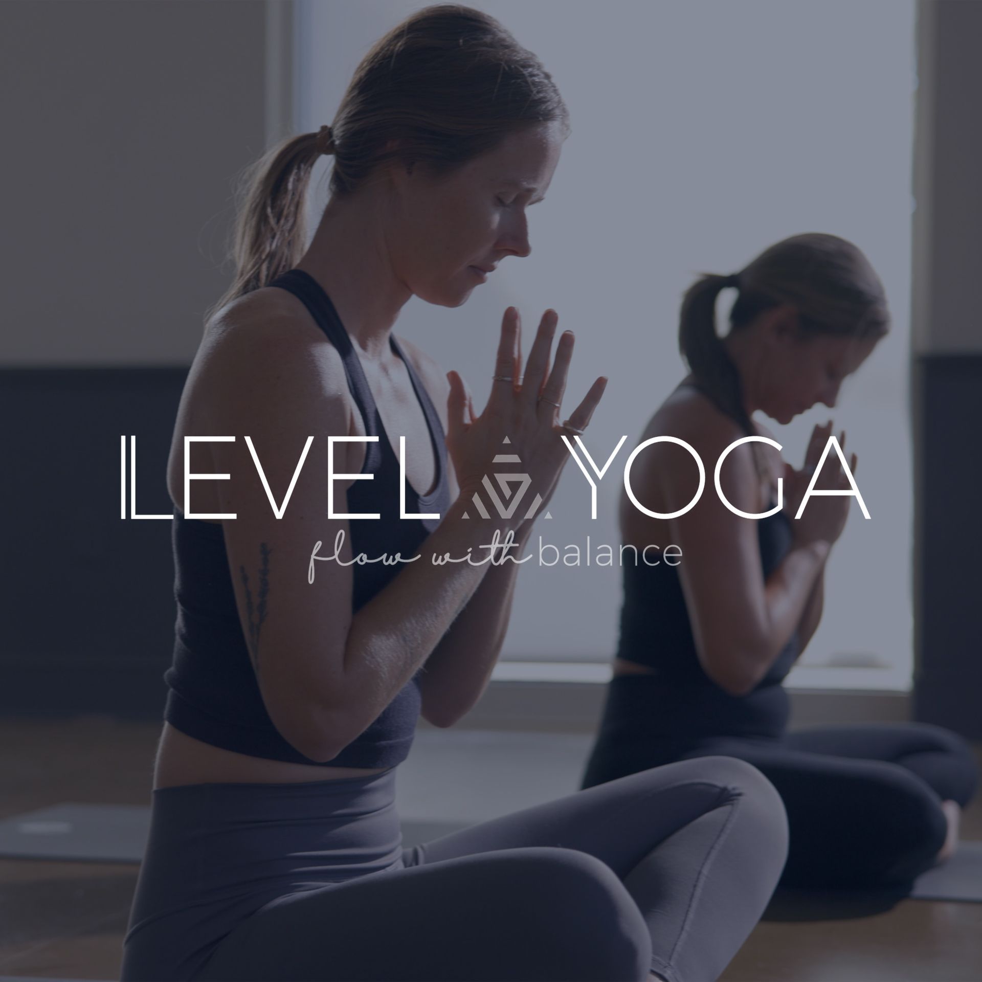 Two women are sitting on yoga mats with their hands folded in prayer.