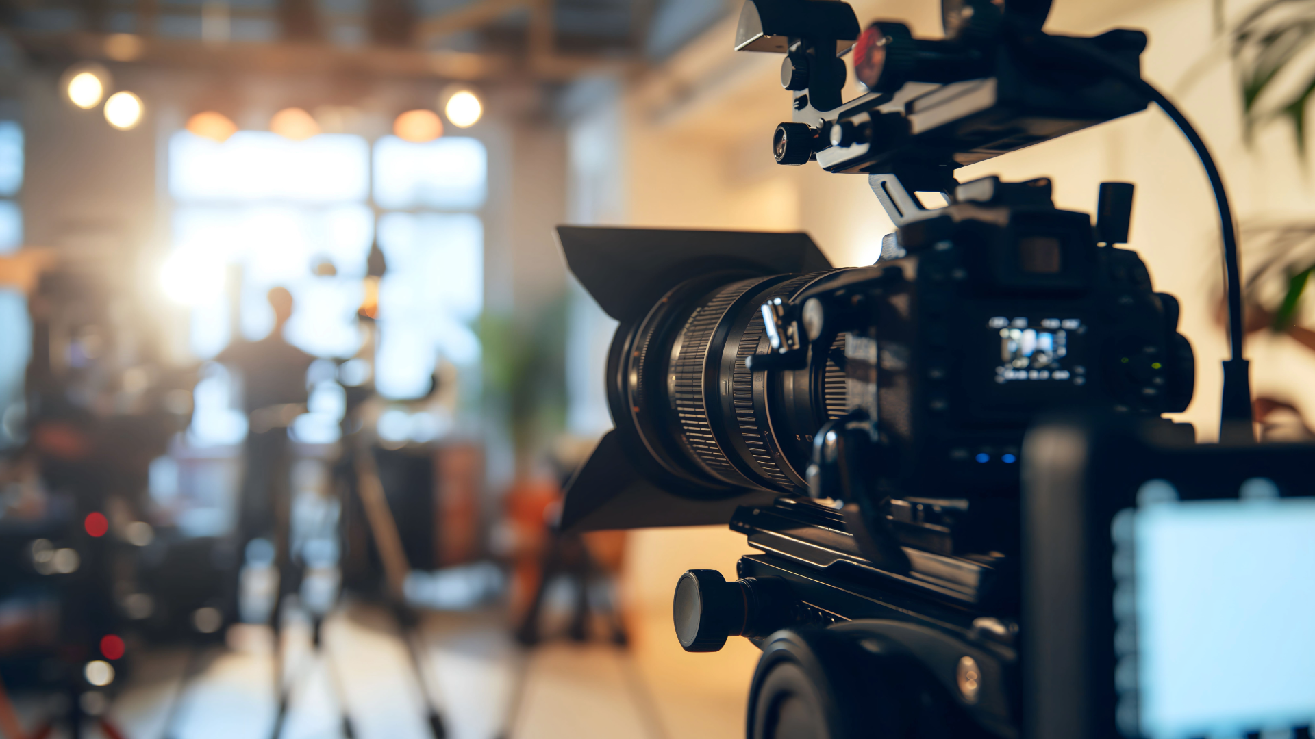 Person holding a camera mounted on a gimbal. The camera is black, with a large lens.  Gray background.