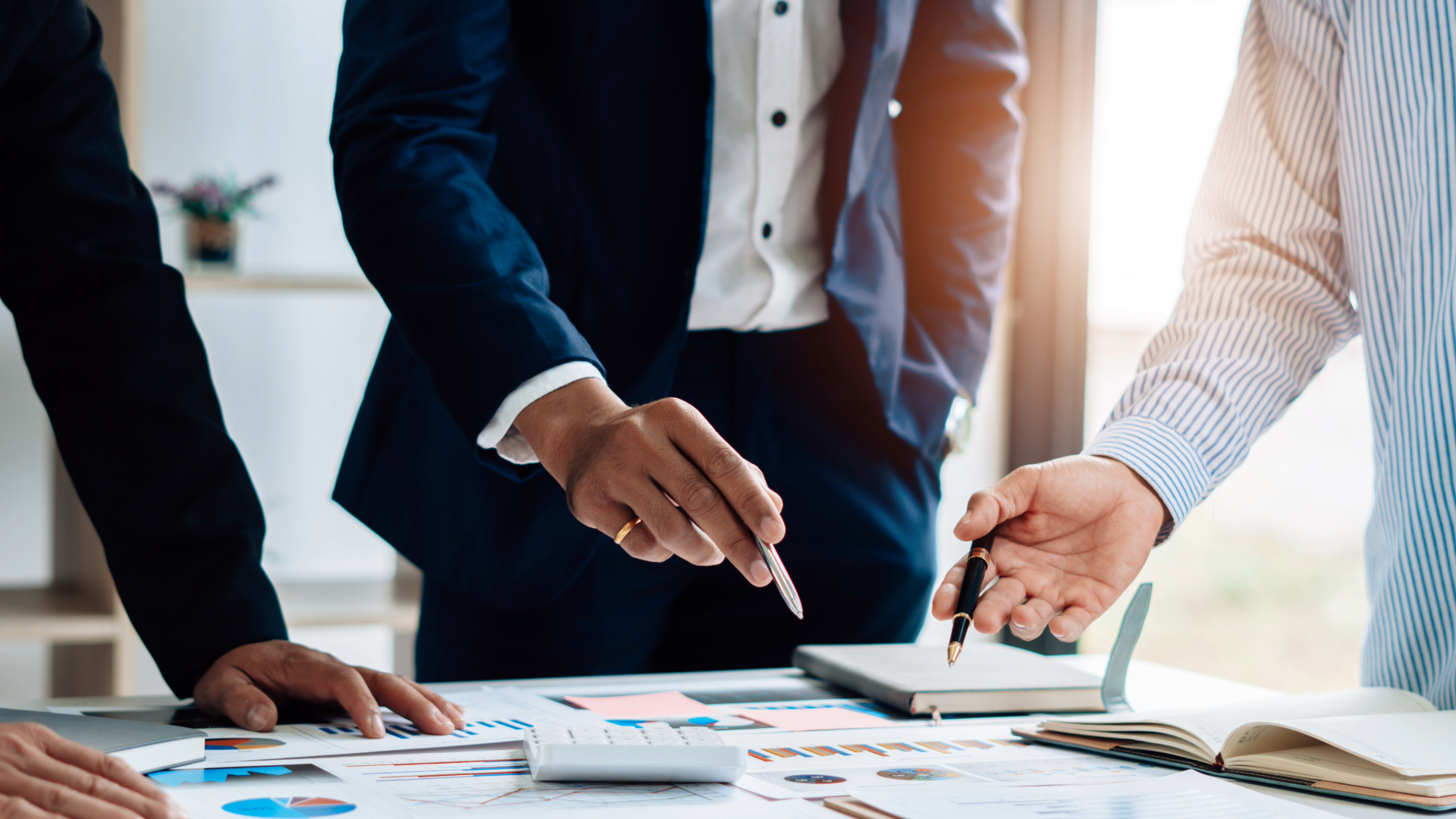 Business professionals in formal attire collaborating over documents and a laptop during a meeting in a bright office.