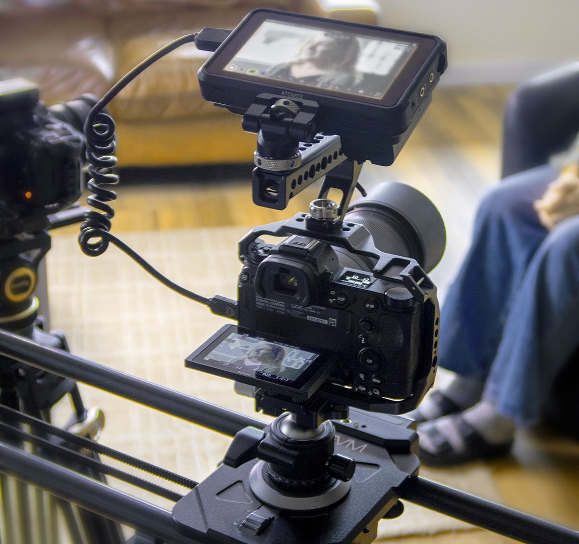 A person holding a camera with a Rode microphone attached, focused on the lens.