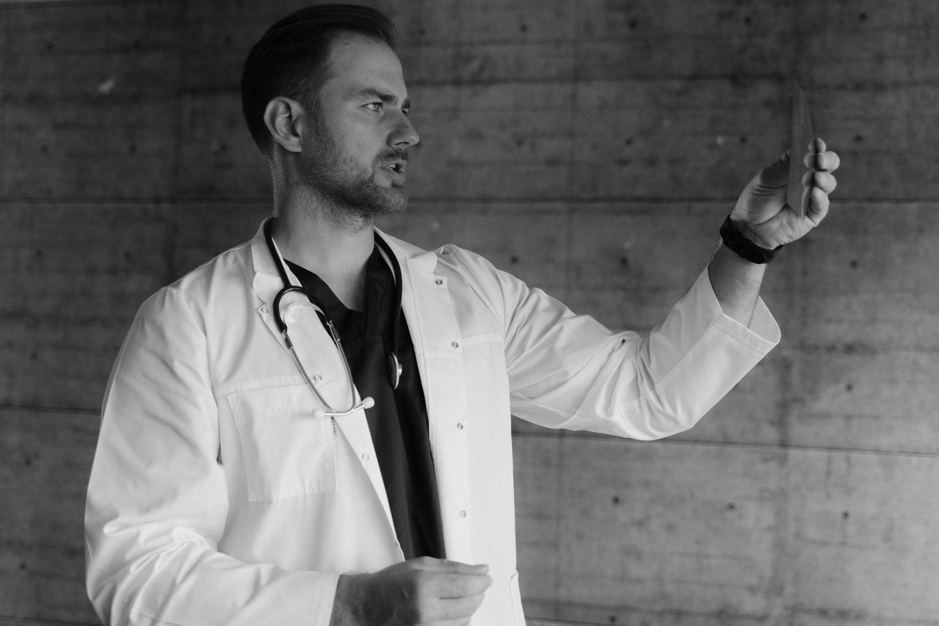 Doctor in white coat demonstrating with a stethoscope against a concrete wall