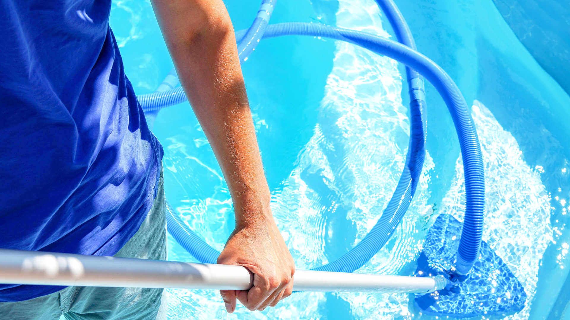 Person cleaning a blue swimming pool with a net and pole.