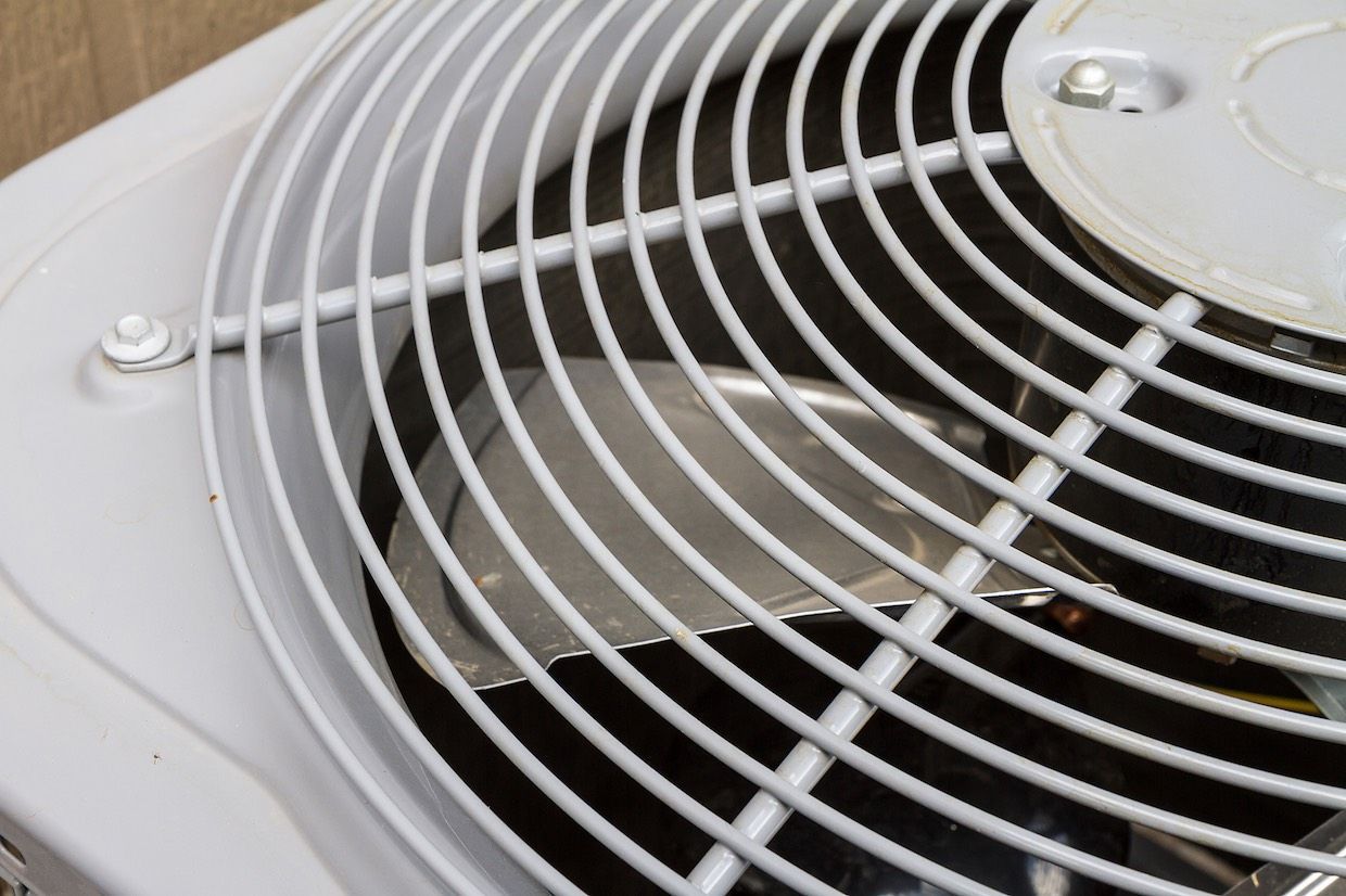 Close-up of a white air conditioner unit fan with a metal grate.