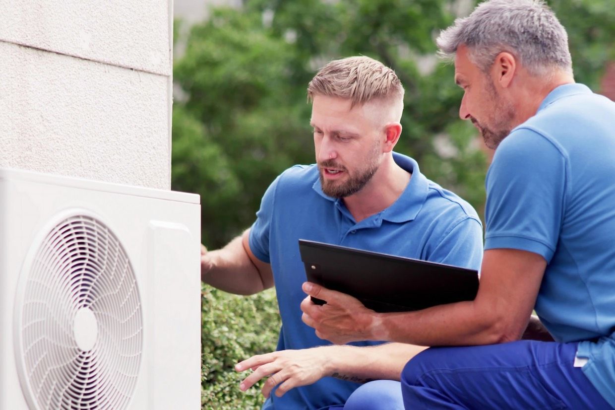 Two men inspecting an HVAC unit outdoors, one holding a clipboard.