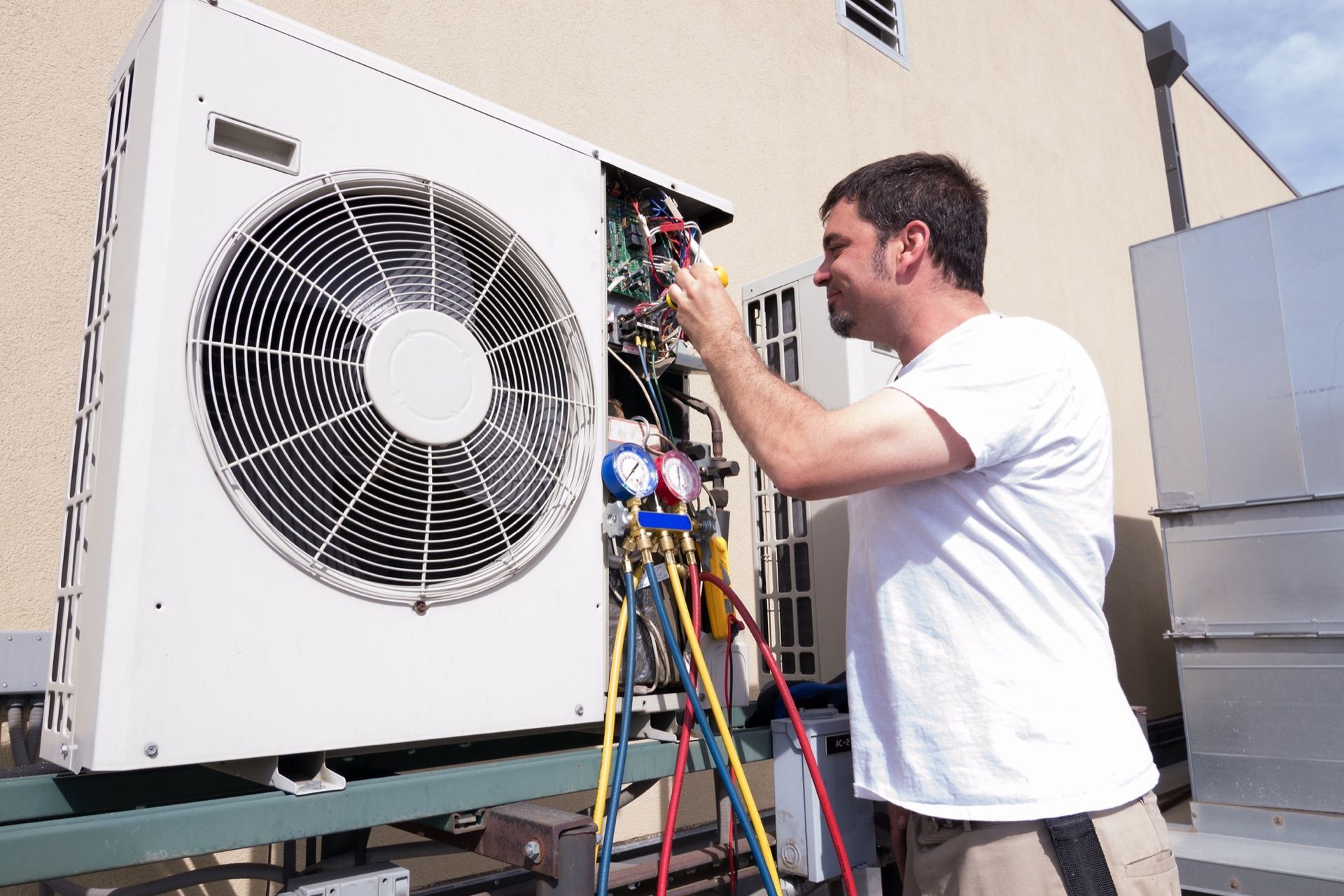 HVAC technician repairs an outdoor air conditioning unit on a rooftop, using tools and gauges.