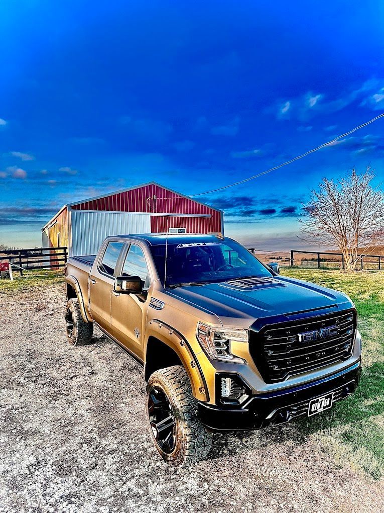 A pickup truck is parked in a gravel lot in front of a barn.