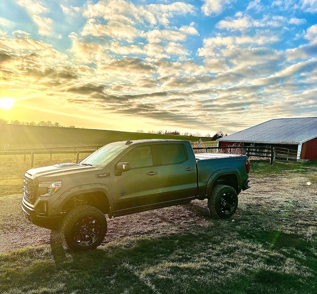 A truck is parked in a field in front of a barn at sunset.