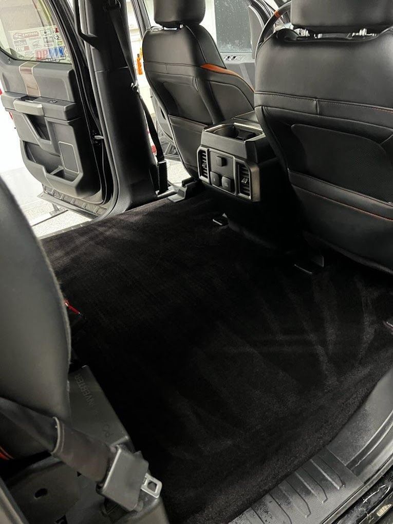 The back seat of a car with a black carpet.