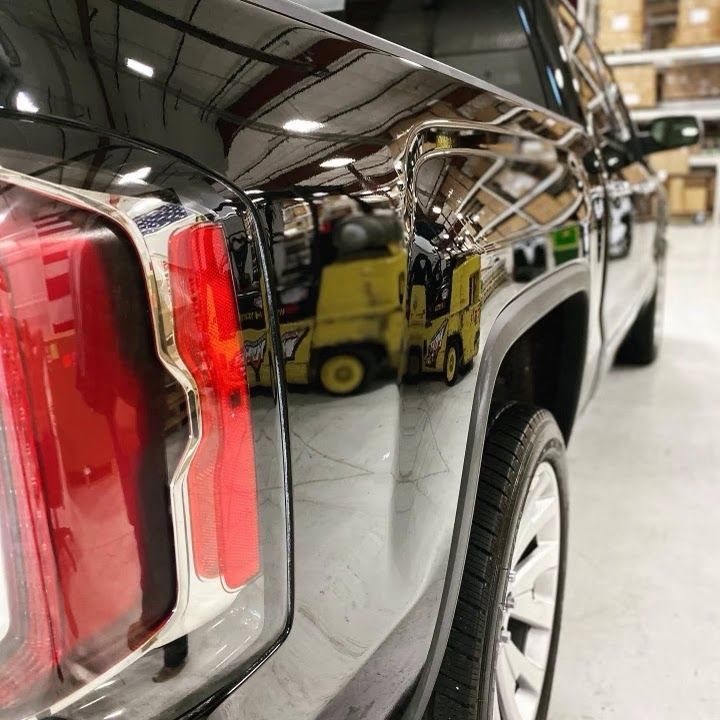 A black truck is parked in a warehouse with a yellow forklift in the background.