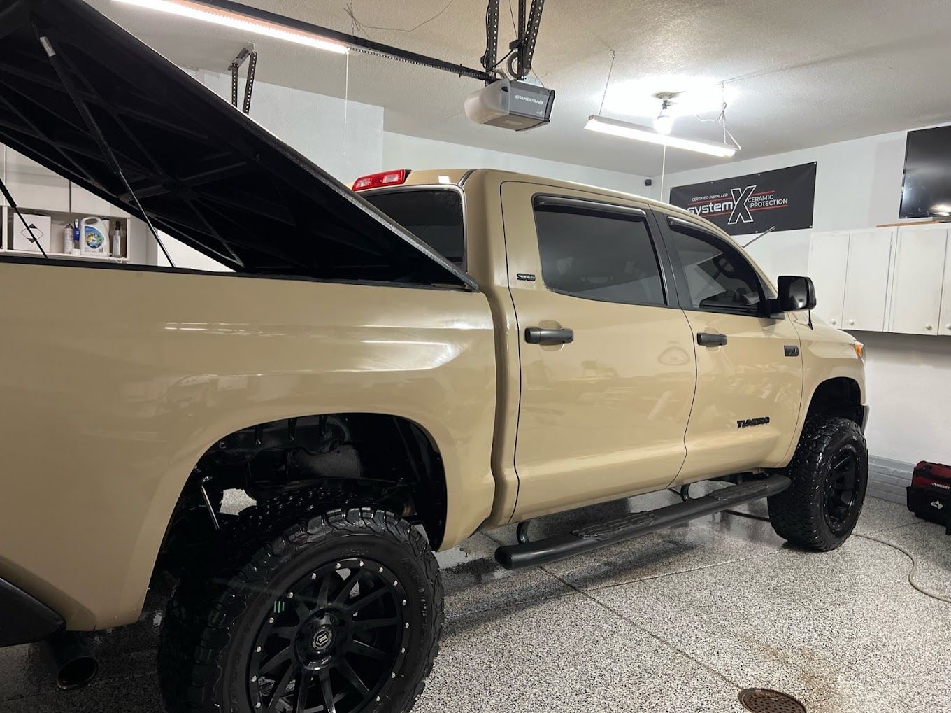 A tan truck with the hood up is parked in a garage.