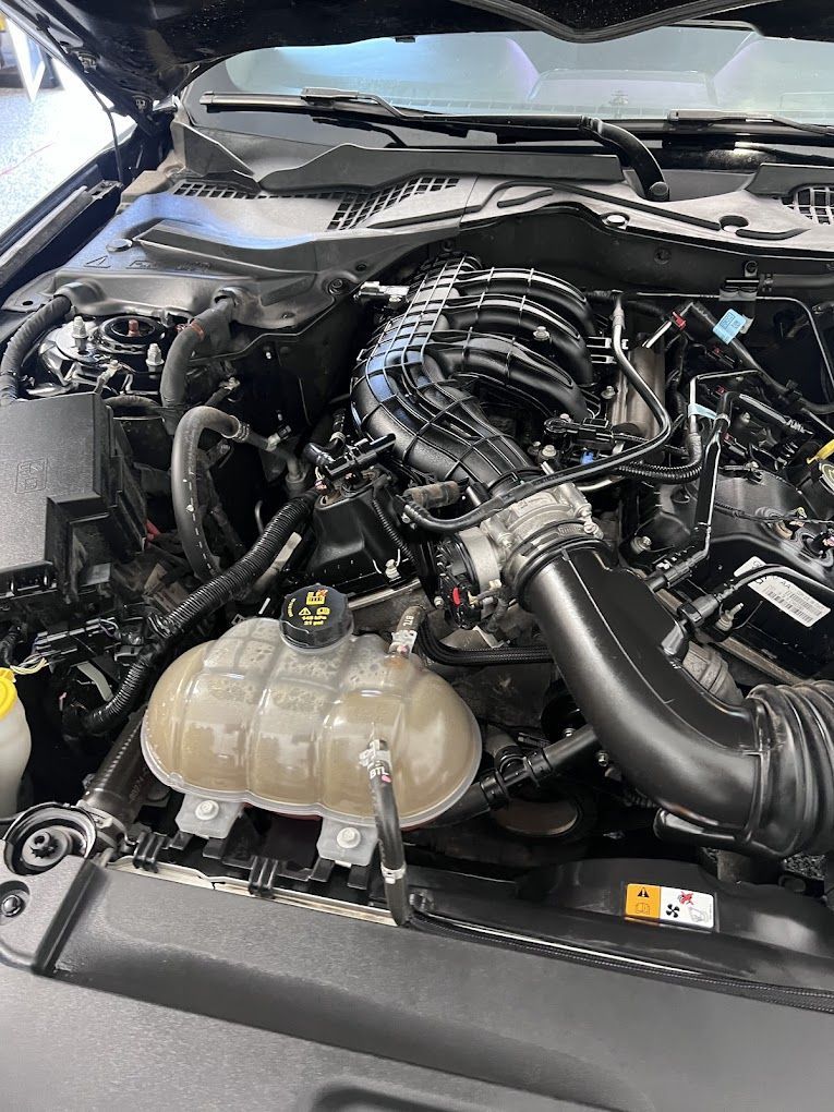 A close up of the engine of a ford mustang with the hood open.