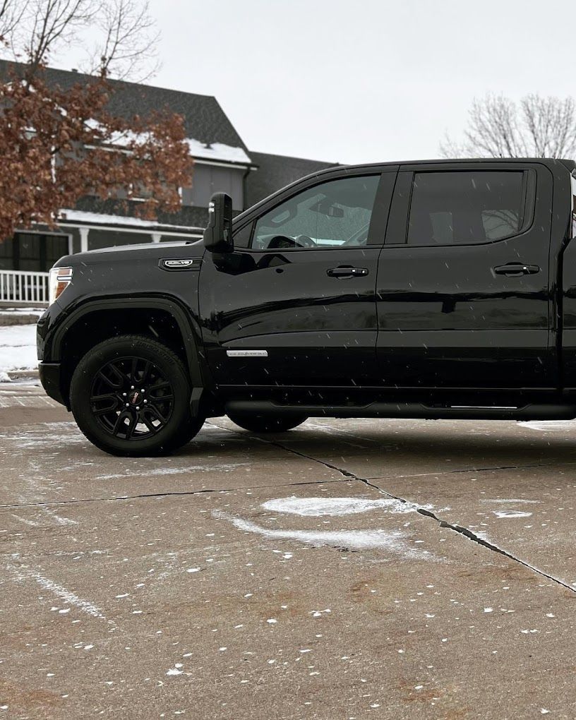 A black truck is parked in a parking lot in front of a house.