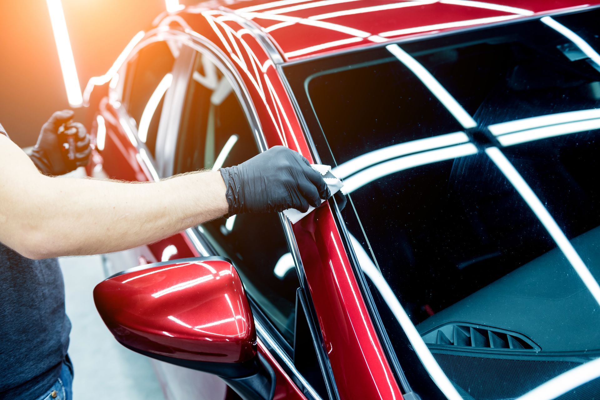 A man is cleaning the windshield of a red car.