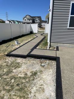 A concrete walkway leading to a house with a white fence.