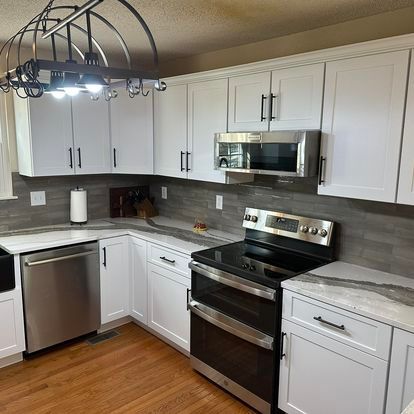 A kitchen with white cabinets , stainless steel appliances , a stove and a microwave.