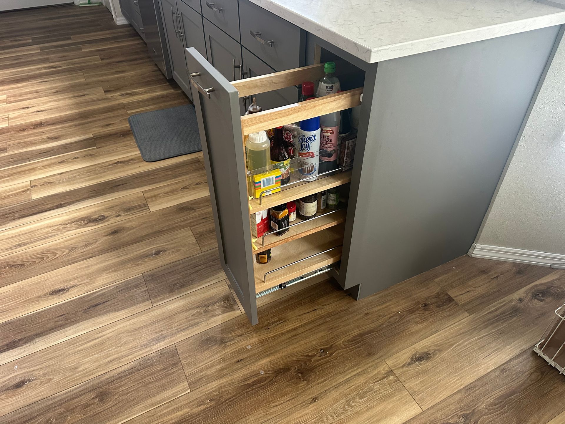 A pull out spice rack in a kitchen with wooden floors.