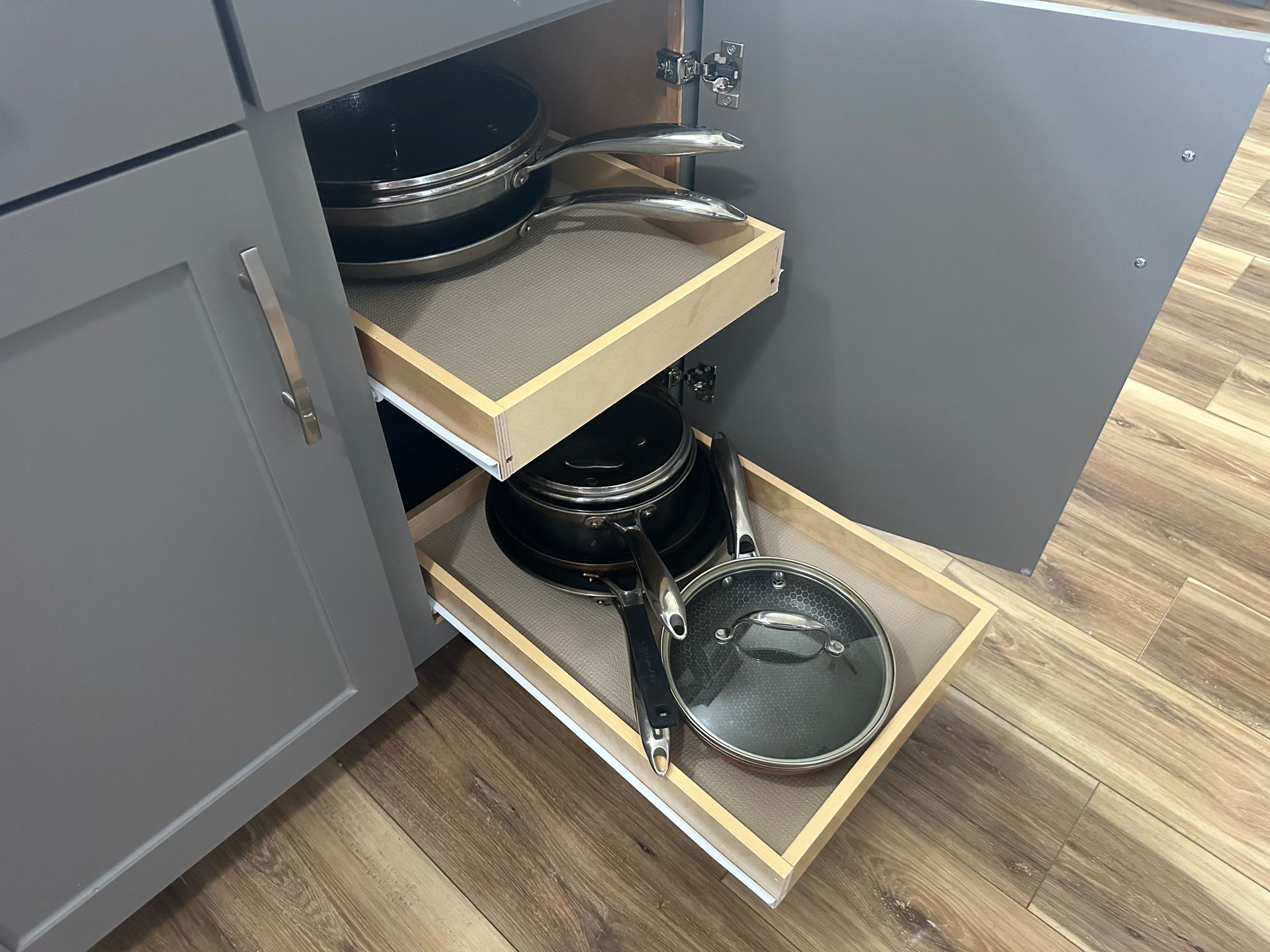 A kitchen with gray cabinets , white counter tops , a sink and a window.