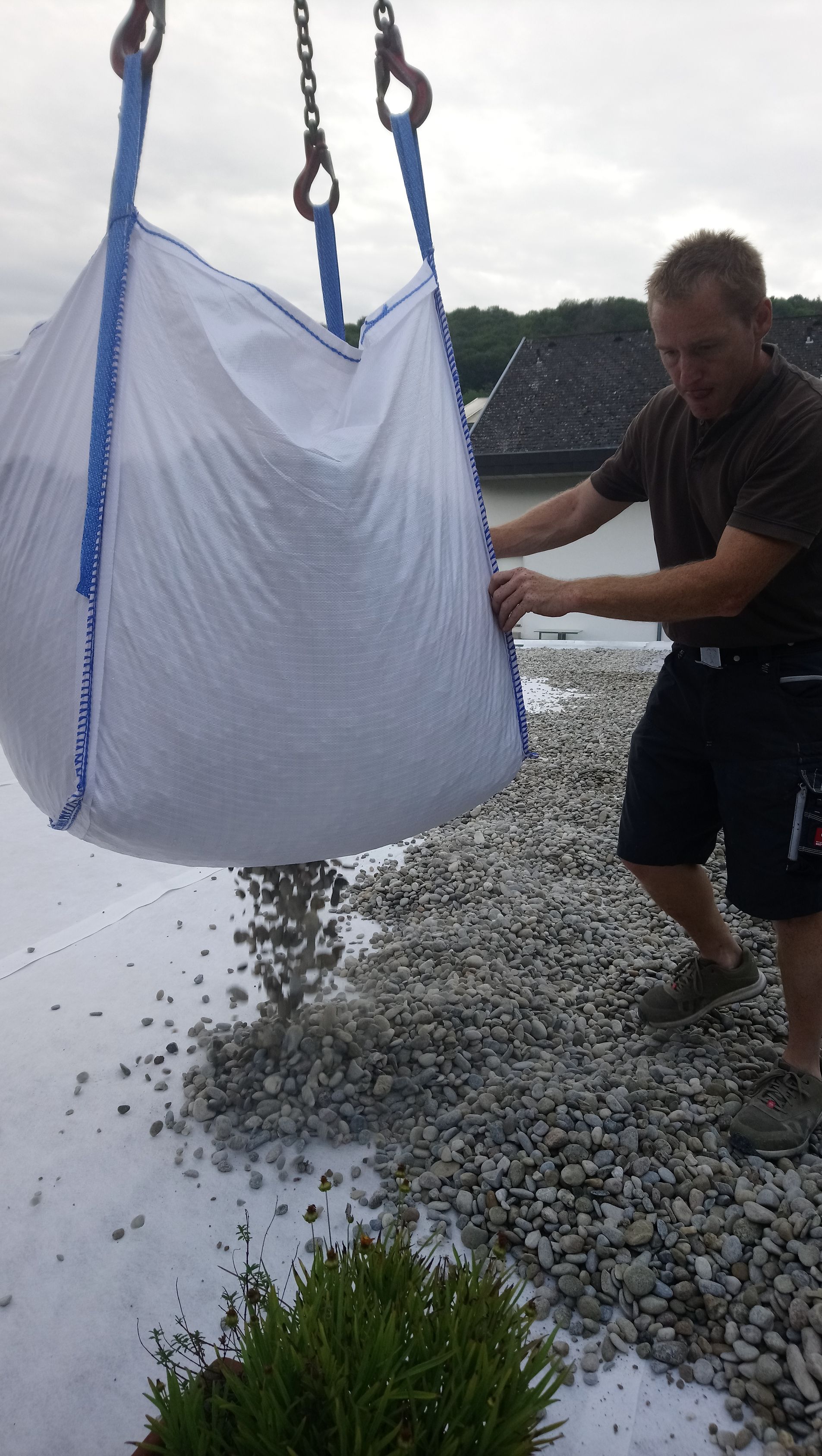 Ein Mann hebt mit einem Kran einen Sack Kies hoch.