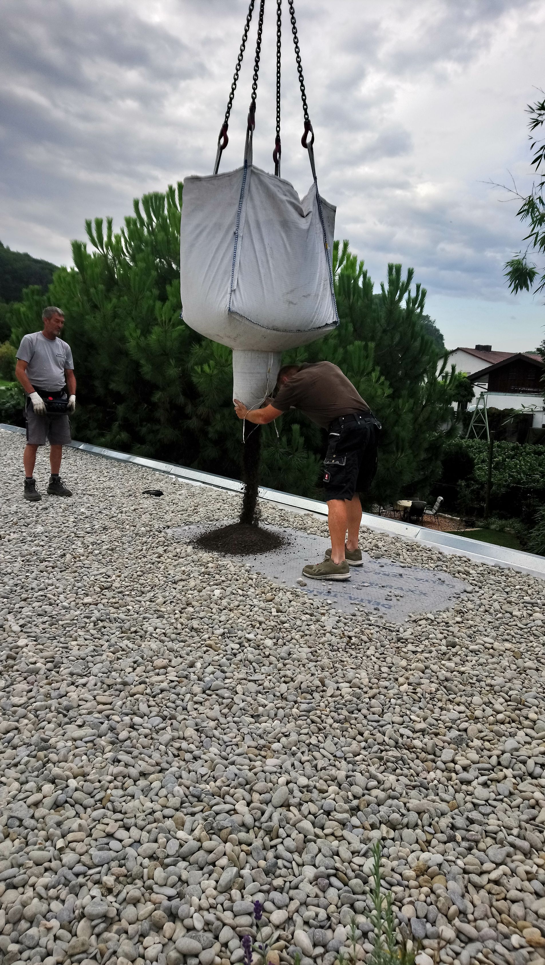 Ein Mann hebt einen Sack Kies auf ein Kiesdach.