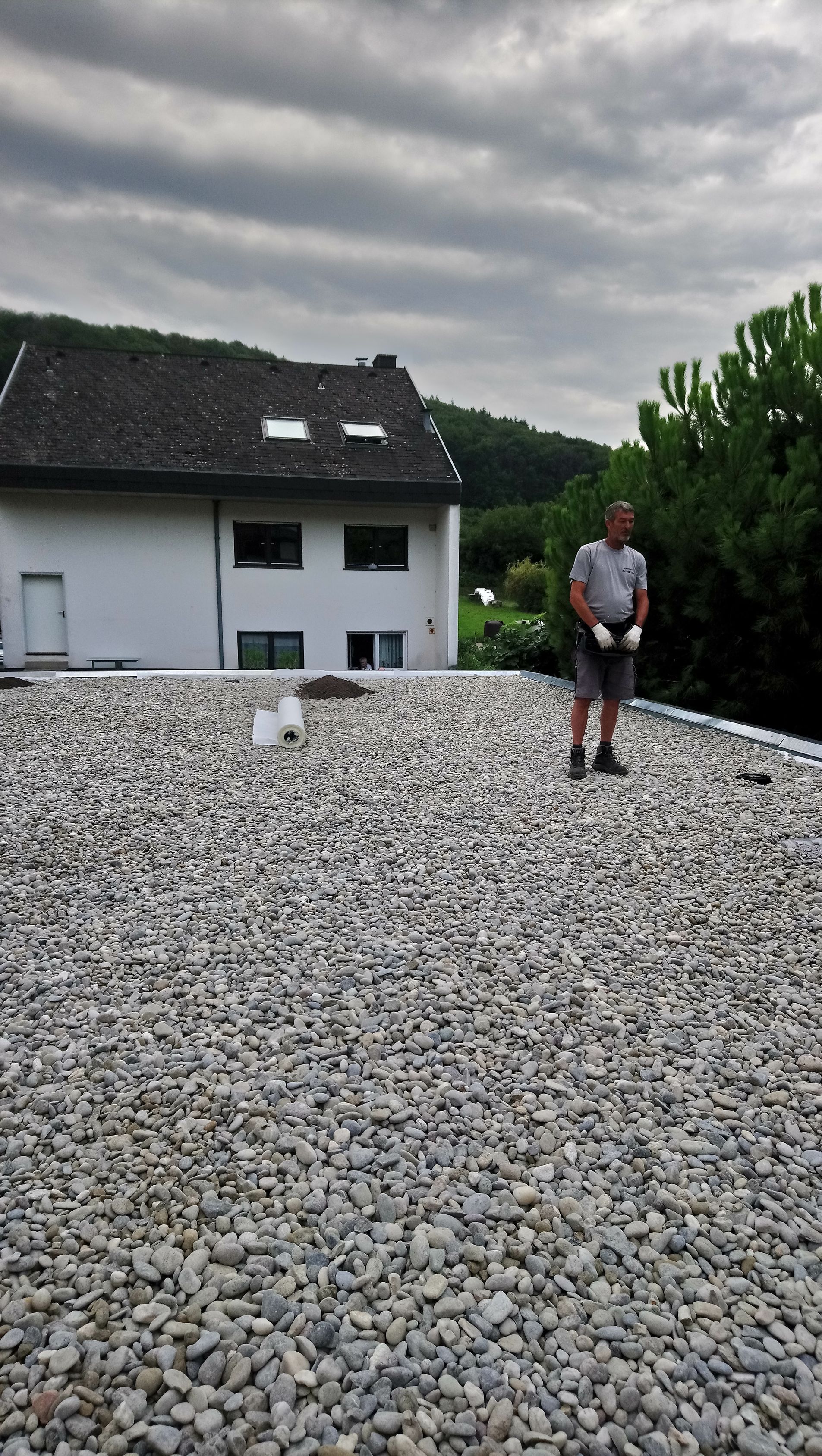 Ein Mann steht auf einem Felsdach vor einem Haus.