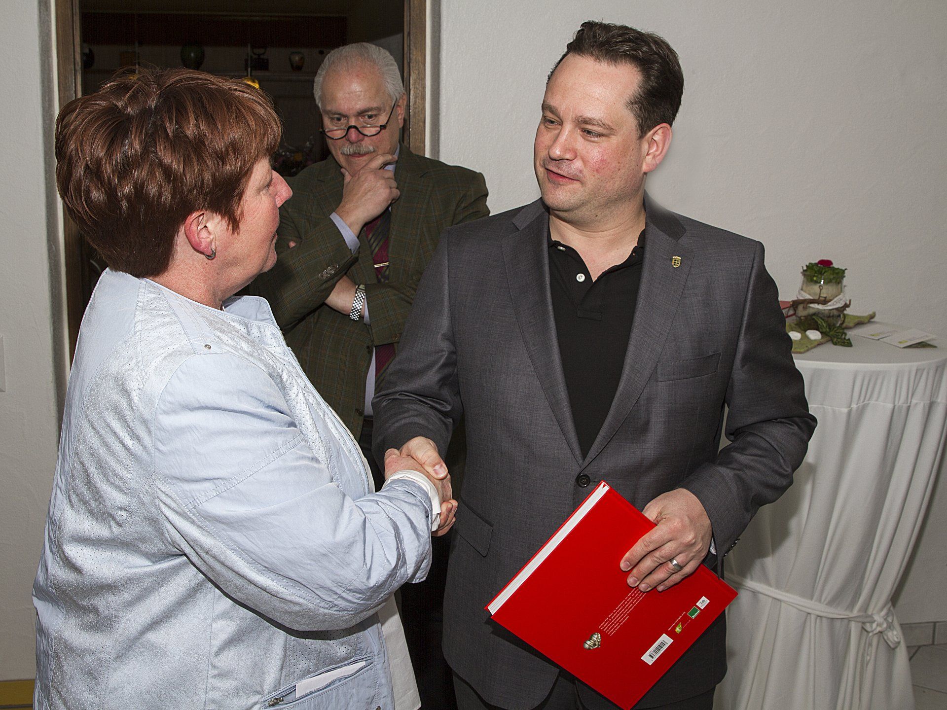 Ein Mann im Anzug schüttelt einer Frau die Hand, die ein rotes Buch hält