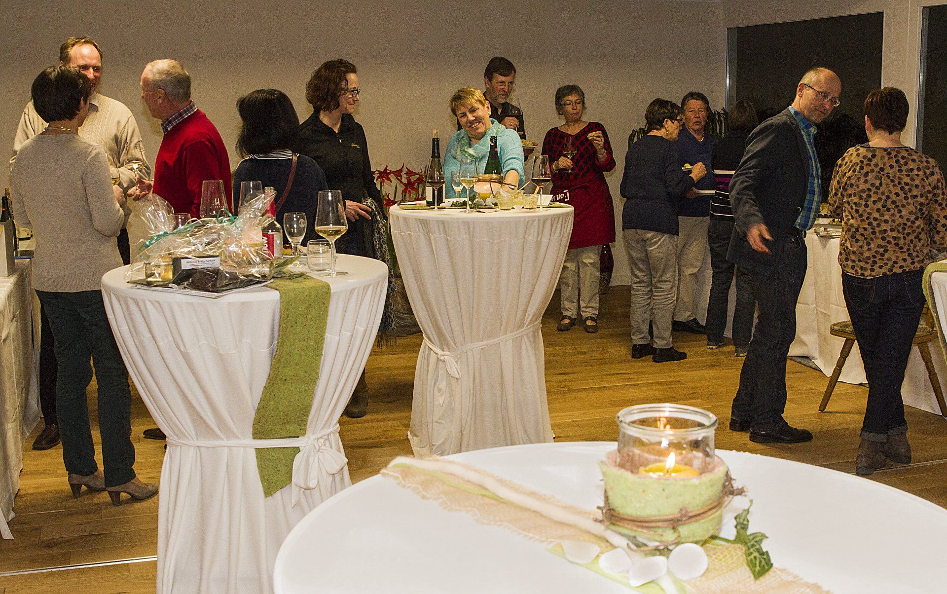 Eine Gruppe von Leuten steht in einem Raum um Tische herum.