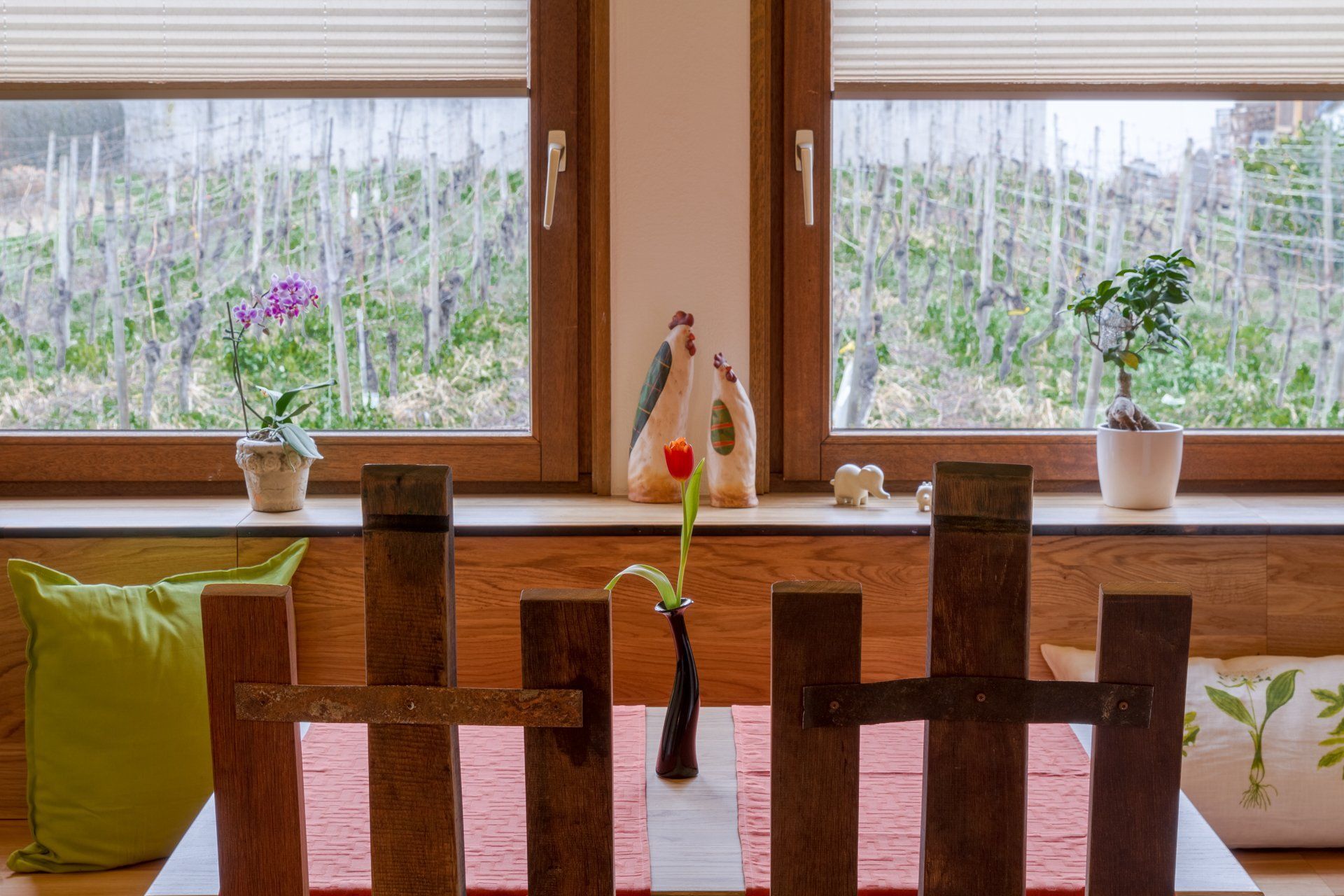 Ein Holztisch mit einer Blumenvase darauf vor einem Fenster.