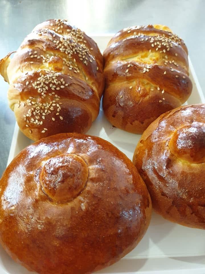 Quattro pagnotte di challah dorate e intrecciate su un vassoio bianco, una delle quali cosparsa di semi di sesamo.