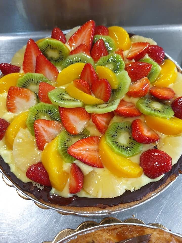 Crostata di frutta con fragole, kiwi e pesche su una base di pasta frolla.