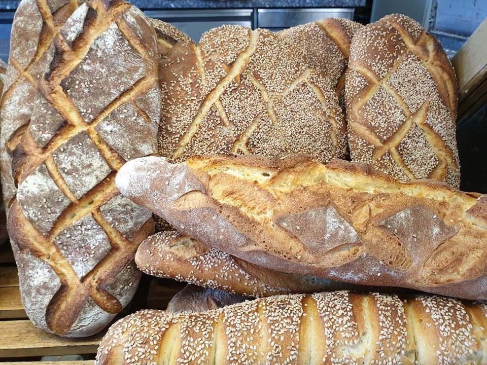 Assortimento di pani artigianali con crosta rigata e semi di sesamo, su vassoi di legno.