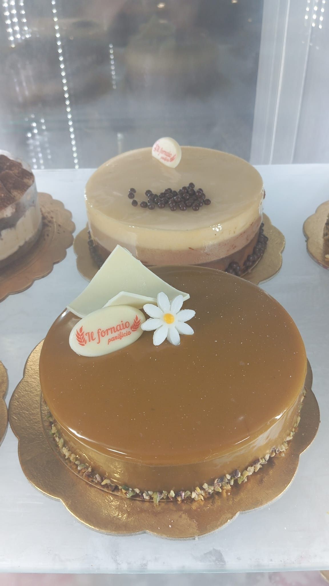 Torte con glassa lucida al caramello e cioccolato esposte in una vetrina da pasticceria.