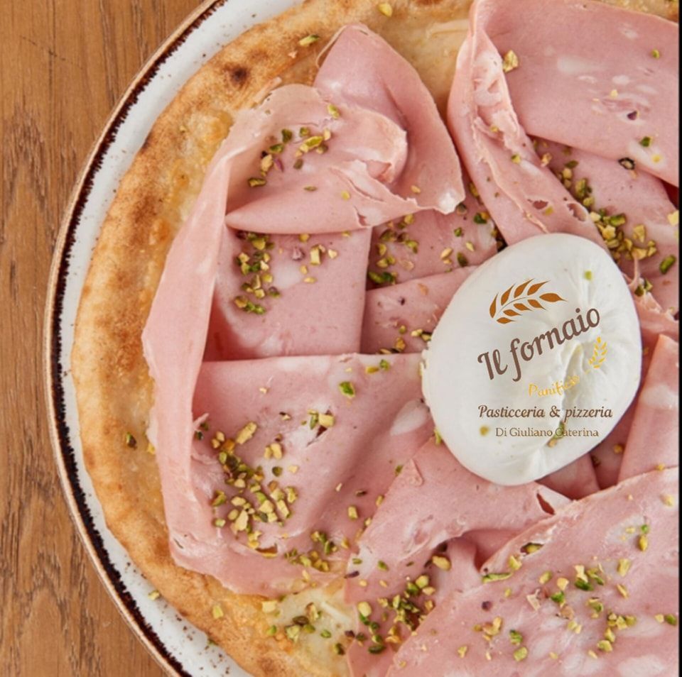 Pizza condita con mortadella, pistacchi e una pallina bianca di formaggio; su un piatto rustico.