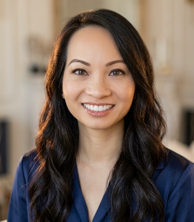 Smiling woman with long dark hair in a navy blouse against a softly blurred indoor background