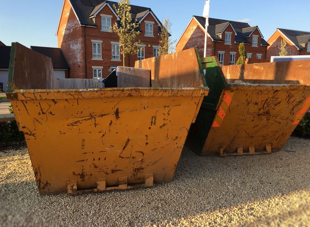Two Yellow Dumpsters Are Sitting on Gravel in Front of a Row of Houses — Gardners Yamba Skip Bin Hire in Townsend, NSW