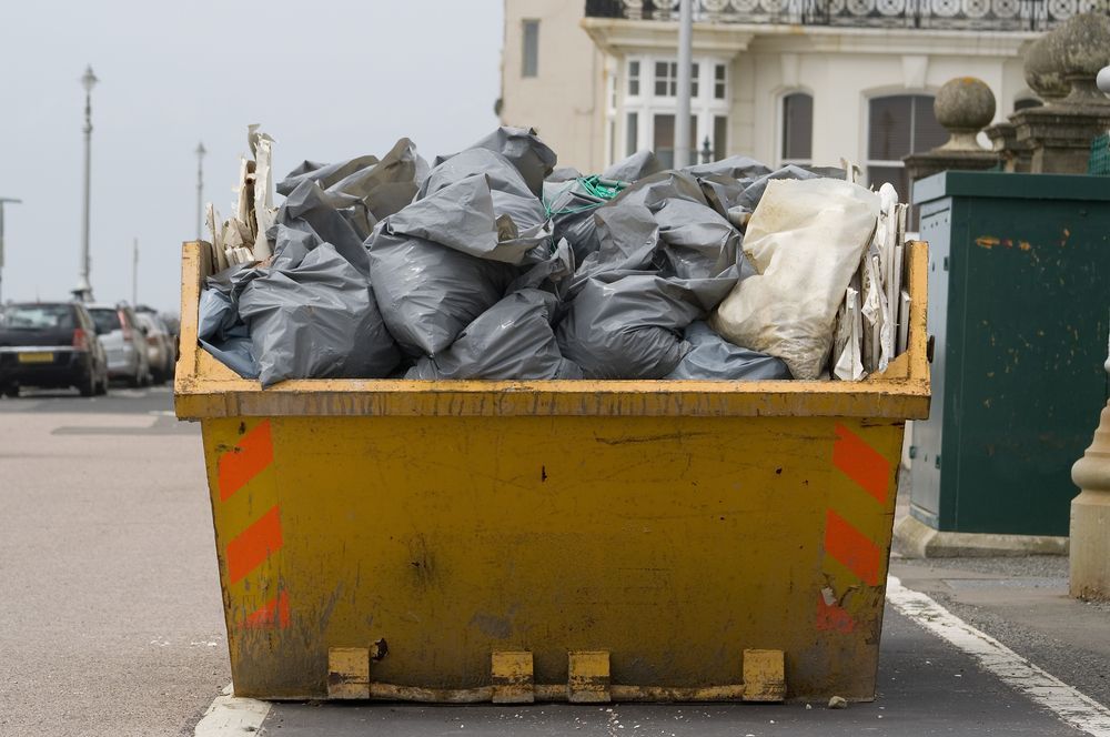 A Yellow Dumpster Filled With Garbage Bags is Parked on the Side of the Road — Gardners Yamba Skip Bin Hire in Grafton, NSW
