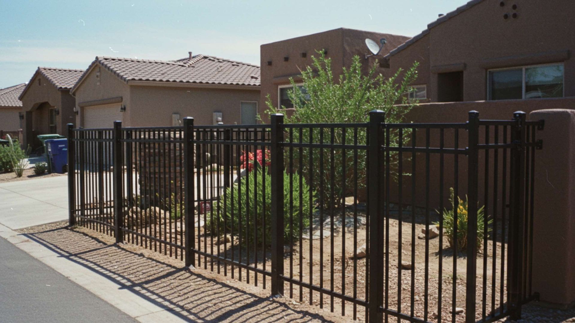 Black metal fence separating yards in a residential neighborhood on a sunny day.